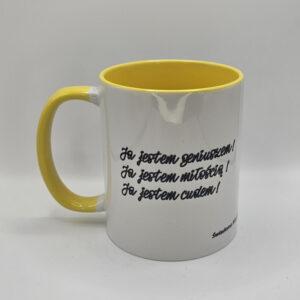 Kubek biały z żółtym wnętrzem i uszkiem z afirmacjami po obydwu stronach.